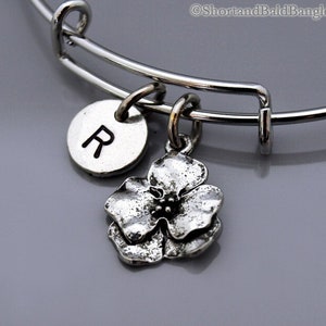 May include: A silver charm bracelet with a flower charm and a round charm with the letter "R" engraved on it.