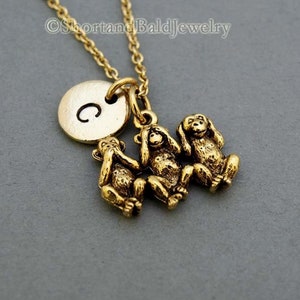 Puede incluir: Collar de oro con un dije redondo que dice "C" y tres dijes de mono de oro. Los monos están en la pose "no veas el mal, no escuches el mal, no hables el mal".