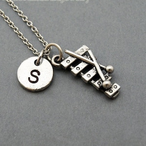May include: Silver necklace with a xylophone charm and a round charm with the letter 'S' on it.