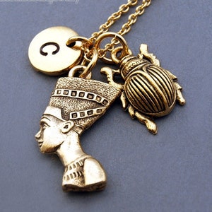 K&ouml;nnte beinhalten: Goldkette mit einem Anh&auml;nger einer &auml;gyptischen K&ouml;nigin, einem Skarab&auml;us-Anh&auml;nger und einem goldenen Initialanh&auml;nger mit dem Buchstaben C.