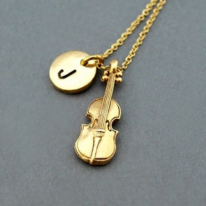 May include: Gold necklace featuring a small violin charm and a round charm with the letter J.