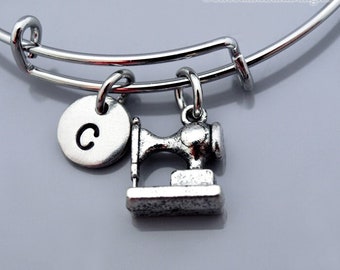 Op de afbeelding: Een zilveren armband met een naaimachinebedel en een bedel met de letter C.