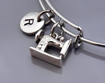 Op de afbeelding: Een zilveren armband met een naaimachinebedel en een zilveren bedel met de letter R.