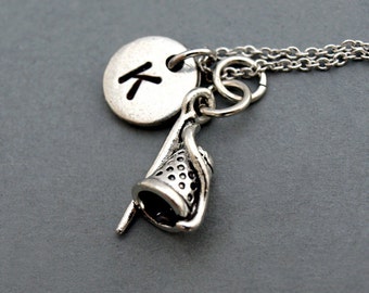 Puede incluir: Collar de plata con un dije de dedal y un dije redondo con la letra K.