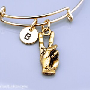 Op de afbeelding: Gouden armband met een vredestekenbedel en een bedel met de letter B.