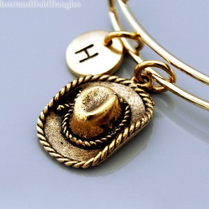 May include: Gold charm bracelet with a gold cowboy hat charm and a gold initial charm with the letter H.