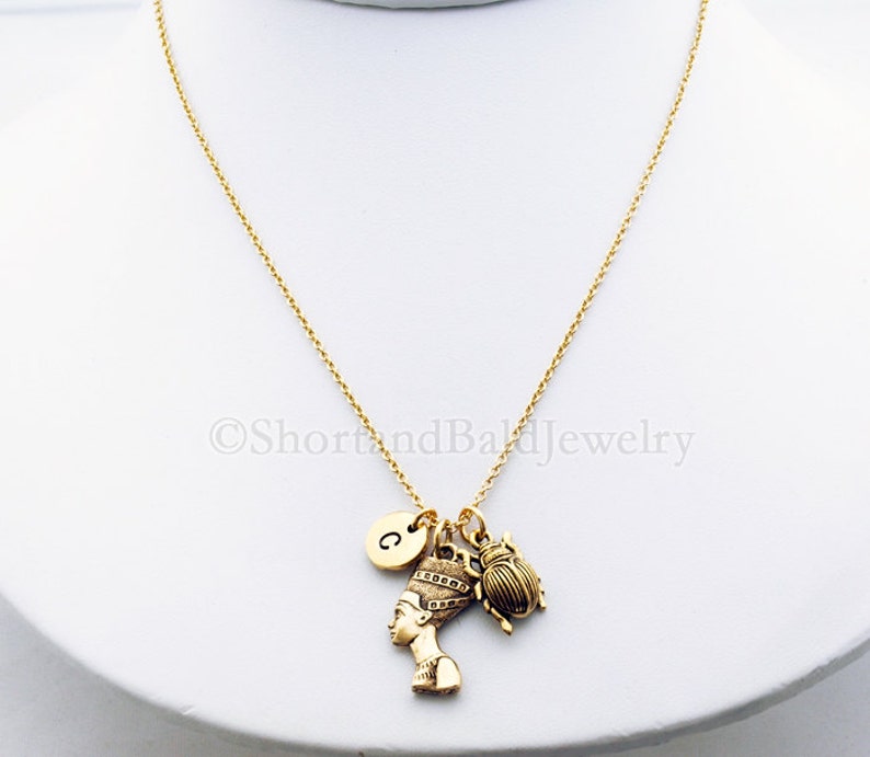 K&ouml;nnte beinhalten: Goldkette mit einem Anh&auml;nger einer &auml;gyptischen K&ouml;nigin, einem Skarab&auml;us und einem Buchstaben 'C' Anh&auml;nger.
