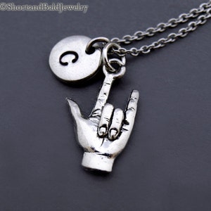 May include: Silver necklace with a charm of a hand making the American Sign Language sign for 'I love you' and a round charm with the letter 'C' on it.