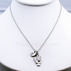 May include: Silver necklace with a charm of a hand making the sign for 'I love you' in American Sign Language. The necklace also has a small charm with the letter 'C' on it.