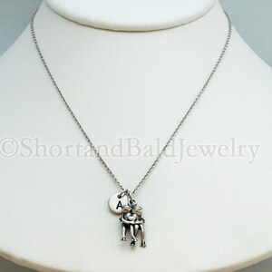 May include: Silver necklace with a charm of two people holding each other and a small round charm with the letter A.