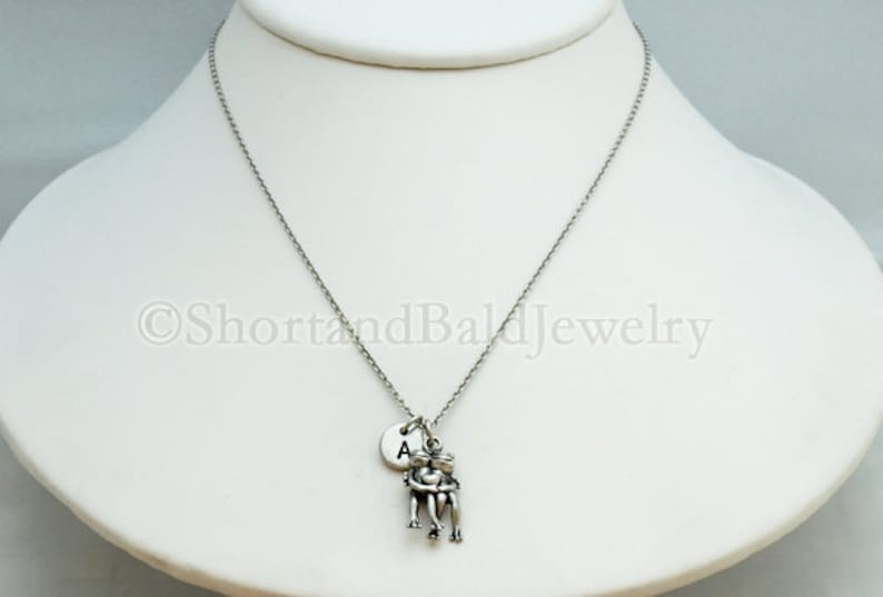 May include: Silver necklace with a charm of two people holding each other and a small round charm with the letter A.