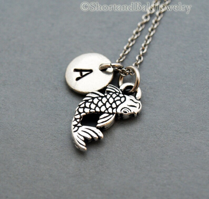 May include: Silver necklace with a silver charm of a koi fish and a silver disc charm with the letter A.