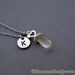 May include: Silver necklace with a clear glass pacifier charm and a silver disc charm with the letter K.