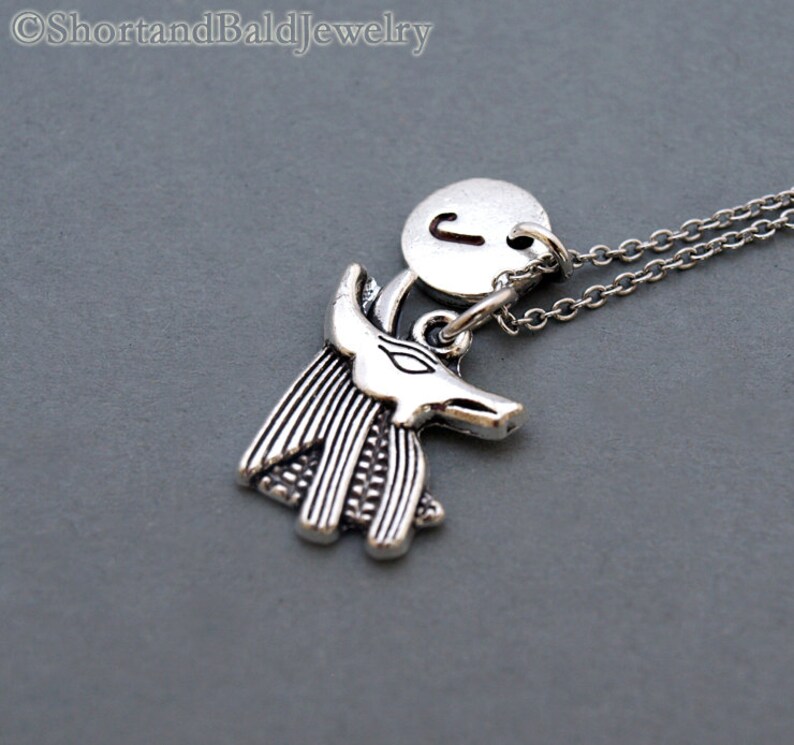 May include: Silver necklace with a charm of an Anubis head and a round charm with the letter J.