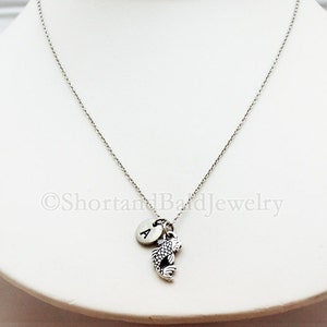 May include: A silver chain necklace with a silver charm of a fish and a silver initial charm with the letter "A".