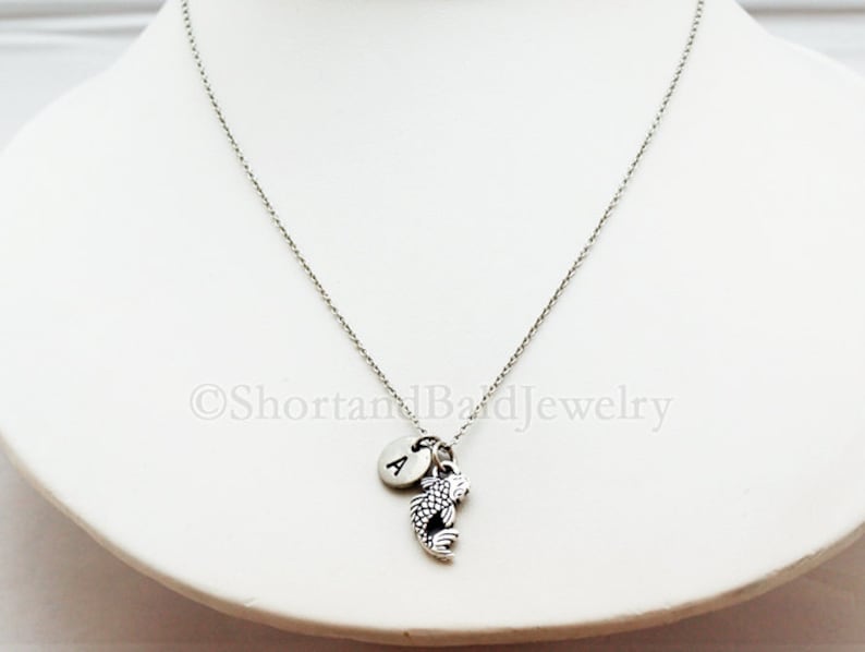 May include: A silver chain necklace with a silver charm of a fish and a silver initial charm with the letter "A".