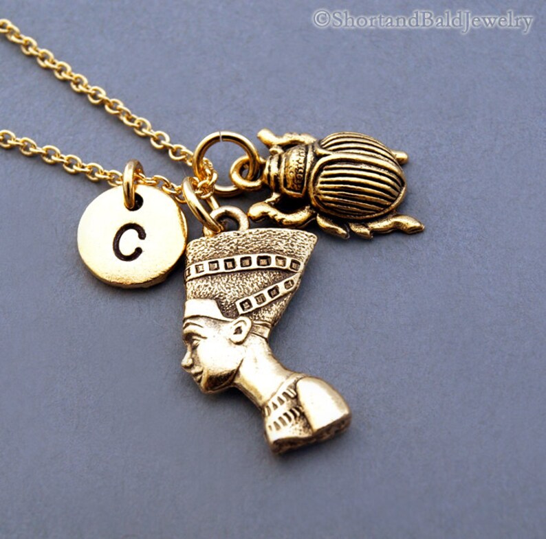 K&ouml;nnte beinhalten: Goldkette mit einem Anh&auml;nger einer &auml;gyptischen K&ouml;nigin, einem Skarab&auml;us und einem Buchstaben C-Anh&auml;nger.