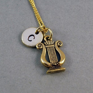 K&ouml;nnte beinhalten: Goldkette mit einem kleinen runden Anh&auml;nger, der mit dem Buchstaben "C" graviert ist, und einem Lyra-Anh&auml;nger.