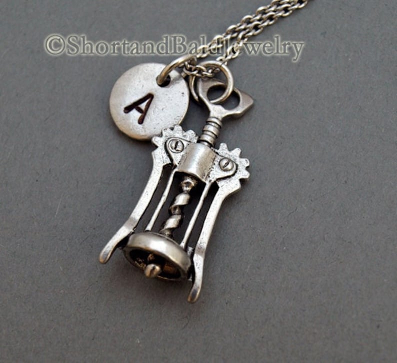 May include: Silver necklace with a corkscrew charm and a round charm with the letter A.
