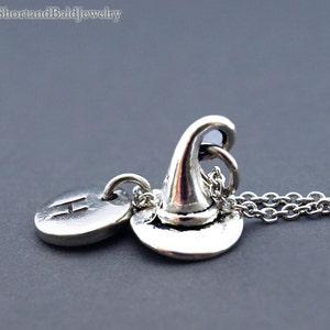 Puede incluir: Collar de plata con un dije de sombrero de bruja y un dije inicial personalizado. El dije inicial es un círculo con la letra "H" grabada en él.