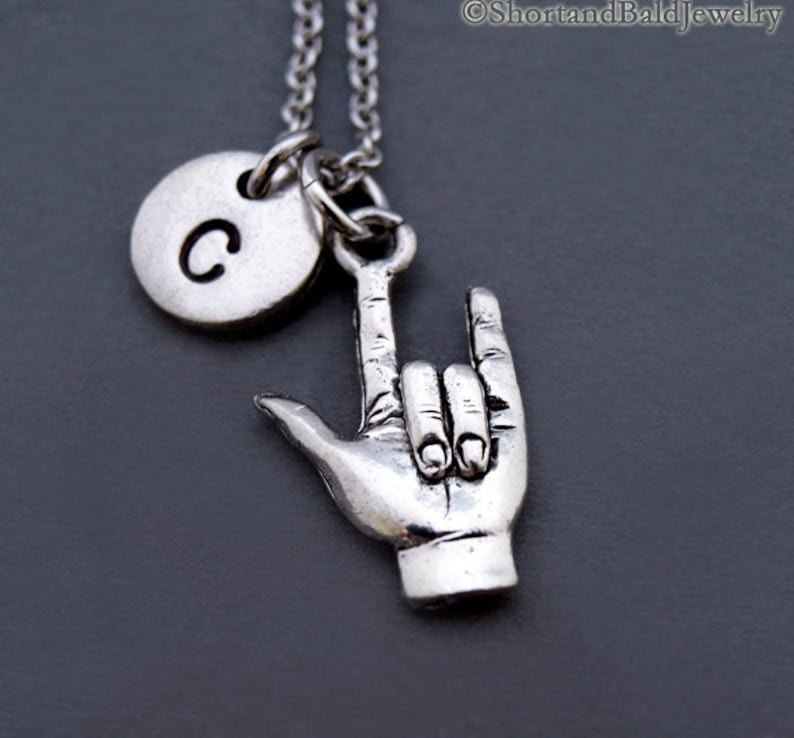 May include: Silver necklace with a charm of a hand making the American Sign Language sign for 'I love you' and a round charm with the letter 'C' on it.