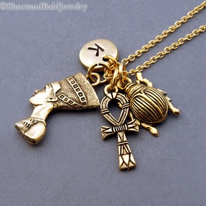 May include: Gold necklace with multiple charms, including an Egyptian queen profile, an ankh, a scarab beetle, and a round charm with the letter "K" on it.