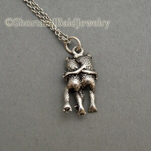 May include: Silver necklace with a pendant of two frogs hugging each other.