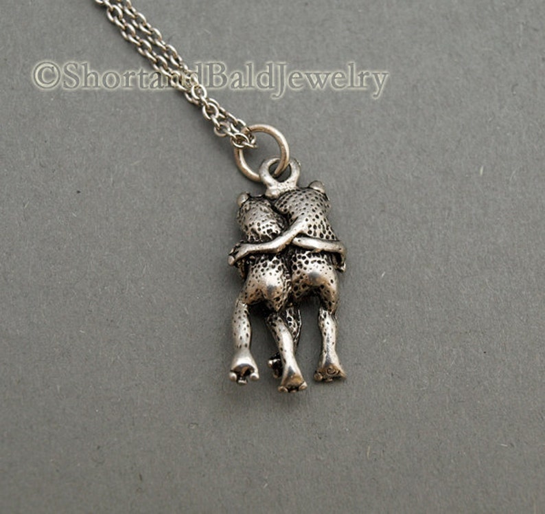 May include: Silver necklace with a pendant of two frogs hugging each other.