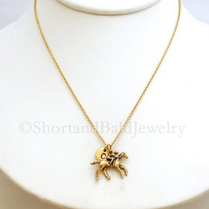 May include: A gold chain necklace with a gold horse and rider charm. The charm has a small round disc with the letter "C" on it.