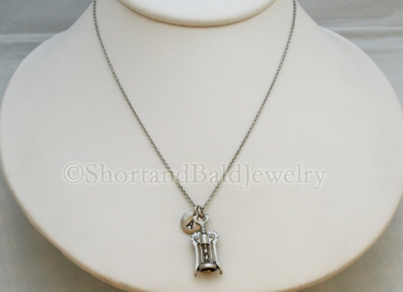 May include: A silver necklace with a corkscrew charm and a small silver charm with the letter A.