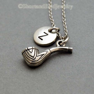 May include: A silver necklace with a pipe charm and a round charm with the letter "Z" on it.