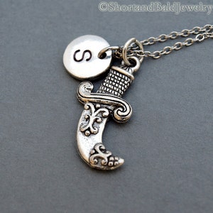May include: Silver necklace with a silver dagger charm and a silver initial charm with the letter "S".