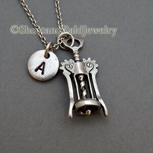 May include: Silver necklace with a corkscrew charm and a small round charm with the letter A engraved on it.