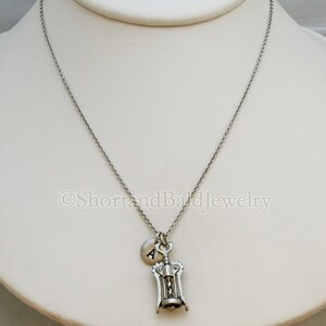 May include: A silver necklace with a corkscrew charm and a small silver disc charm with the letter 'A' on it.