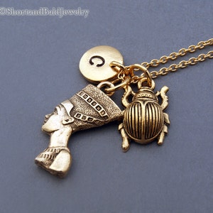 K&ouml;nnte beinhalten: Goldkette mit einem Anh&auml;nger einer &auml;gyptischen K&ouml;nigin, einem Skarab&auml;us und einem goldenen Initialanh&auml;nger mit dem Buchstaben C.