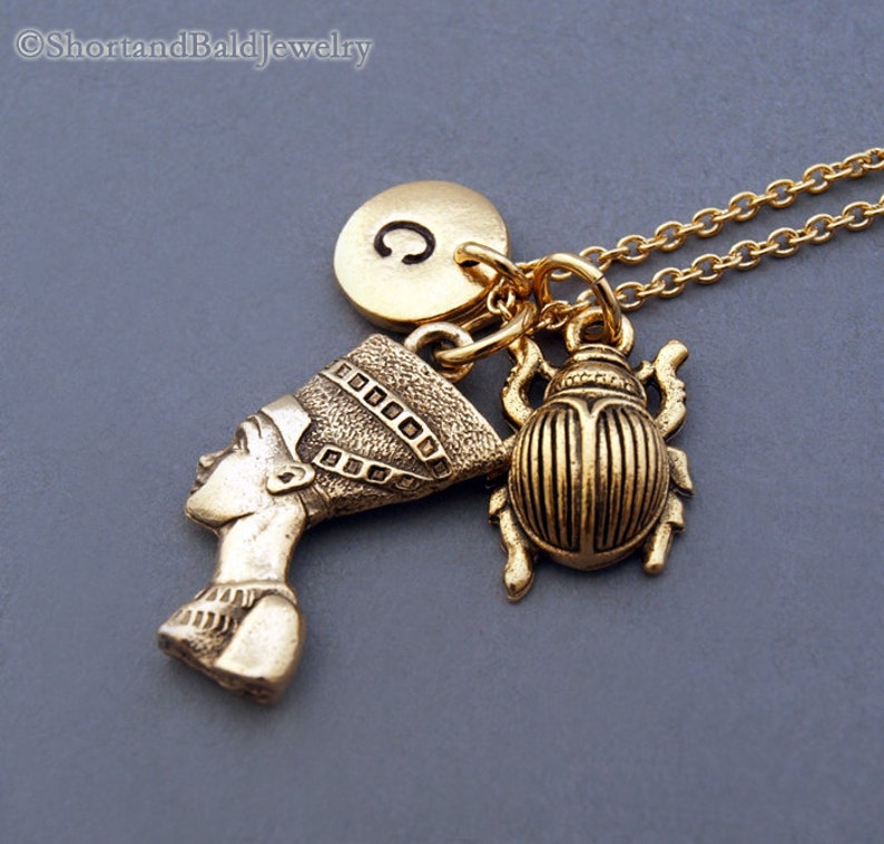 K&ouml;nnte beinhalten: Goldkette mit einem Anh&auml;nger einer &auml;gyptischen K&ouml;nigin, einem Skarab&auml;us und einem goldenen Initialanh&auml;nger mit dem Buchstaben C.