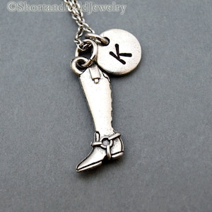 May include: Silver necklace featuring a boot charm and a round charm with the letter K.