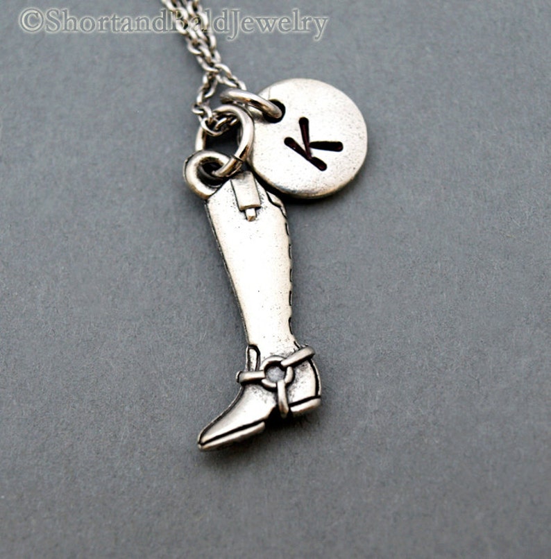 May include: Silver necklace featuring a boot charm and a round charm with the letter K.