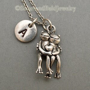 May include: Silver necklace with a charm of two frogs hugging and a silver disc with the letter A engraved on it.