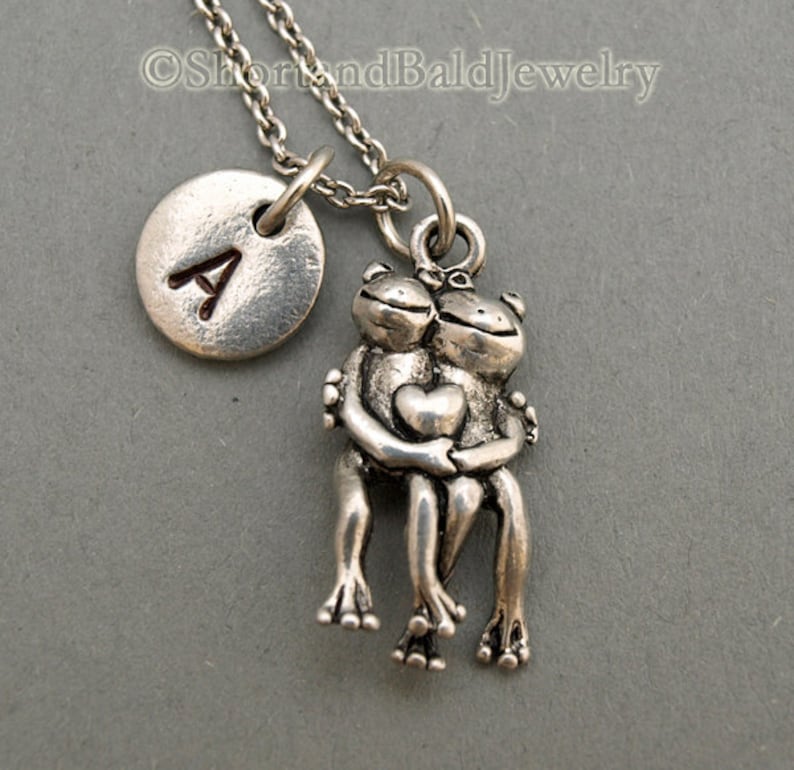 May include: Silver necklace with a charm of two frogs hugging and a silver disc with the letter A engraved on it.