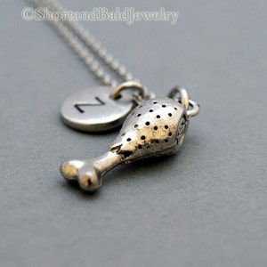 May include: Silver necklace with a charm of a chicken leg and a round charm with the letter Z.