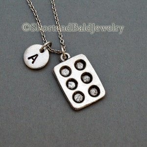 May include: Silver necklace with a letter A charm and a cupcake pan charm.  The necklace is on a gray background.