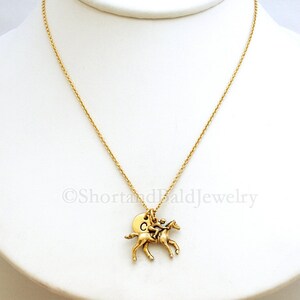 May include: Gold necklace featuring a jockey riding a horse charm and a personalised initial disc charm. The initial disc charm is engraved with the letter "C".