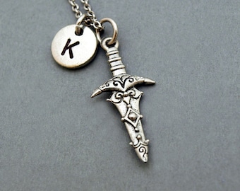 May include: A silver necklace with a silver sword charm and a silver circle charm with the letter K engraved on it.