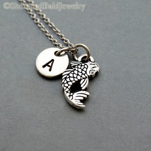 May include: Silver necklace with a small silver fish charm and a silver disc charm with the letter A.