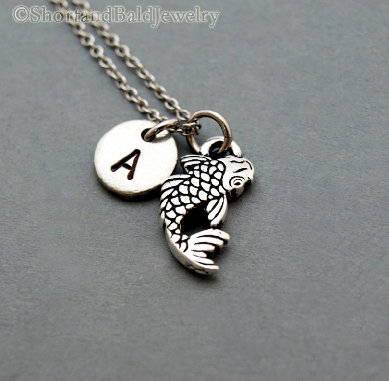 May include: Silver necklace with a small silver fish charm and a silver disc charm with the letter A.