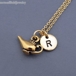 Puede incluir: Collar de oro con un dije de l&aacute;mpara de genio y un dije redondo con la letra "R" en &eacute;l.
