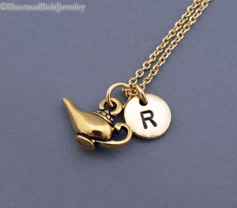 Puede incluir: Collar de oro con un dije de l&aacute;mpara de genio y un dije redondo con la letra "R" en &eacute;l.