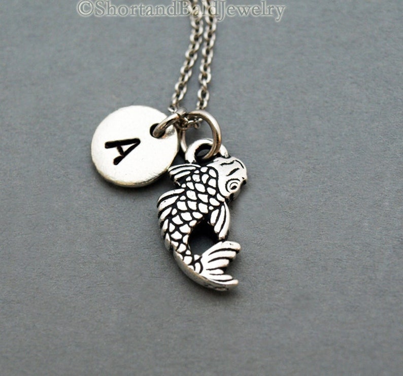 May include: Silver necklace with a silver initial charm and a silver koi fish charm. The initial charm is a letter A.