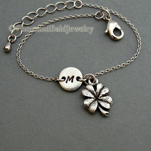 May include: Silver chain bracelet with a silver charm of a four-leaf clover and a silver disc with the letter "M" engraved on it.